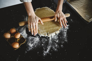 Woman rolling dough by eggs on black background - EYAF01859