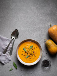 Von oben Schüssel mit köstlichen Kürbissuppe serviert mit Gewürzen in der Nähe von frischen Kürbissen und Löffel auf grauen Tisch im Restaurant - ADSF32944