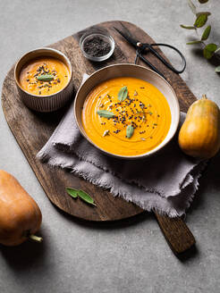 Bowl with delicious pumpkin soup served with seasonings placed near fresh pumpkin on a wooden board on gray table in restaurant - ADSF32945