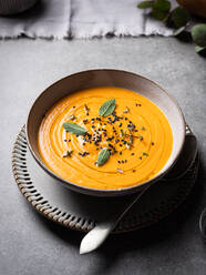 Von oben Schüssel mit köstlicher Kürbissuppe mit Gewürzen auf grauem Tisch in Restaurant serviert - ADSF32946