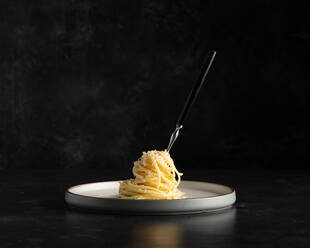 Spaghetti mit geriebenem Käse um eine Gabel gewickelt isoliert auf einem modernen Teller auf einem dunklen Hintergrund - ADSF33020