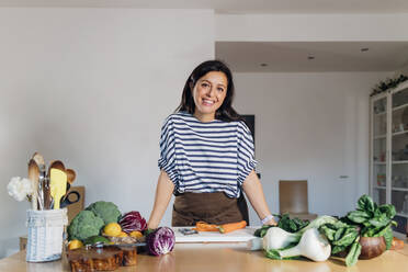 Lächelnde Frau steht am Tisch mit frischem Gemüse - MEUF05073