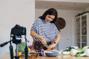 Woman cutting carrot filming through camera at home - MEUF05082