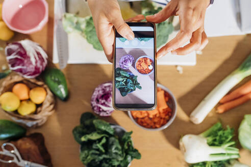 Frau fotografiert frisches Gemüse mit ihrem Smartphone zu Hause - MEUF05085