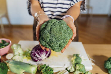 Woman showing fresh broccoli at home - MEUF05093