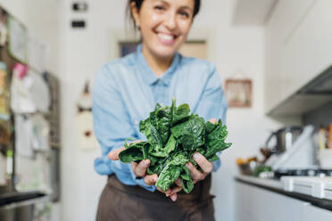 Lächelnde Frau mit frischen Spinatblättern in der Küche zu Hause - MEUF05108