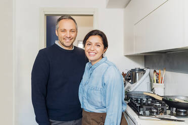 Smiling couple standing together by kitchen counter at home - MEUF05117