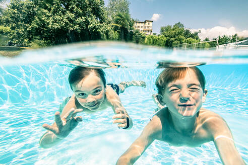 Lächelnde Geschwister schwimmen unter Wasser im Pool an einem sonnigen Tag - WFF00546