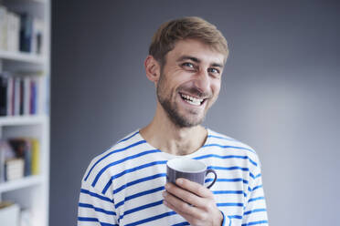 Happy man holding coffee cup at home - FMKF07366