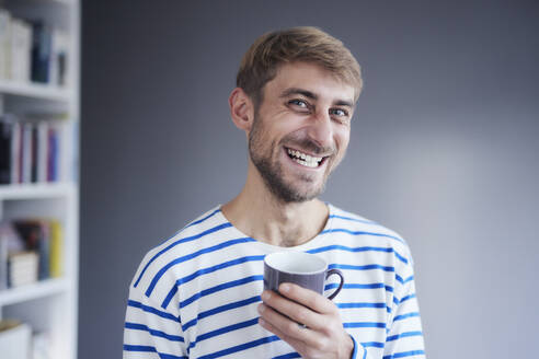 Glücklicher Mann hält Kaffeetasse zu Hause - FMKF07366