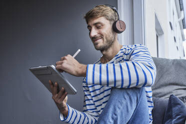 Businessman using tablet PC sitting at home - FMKF07380