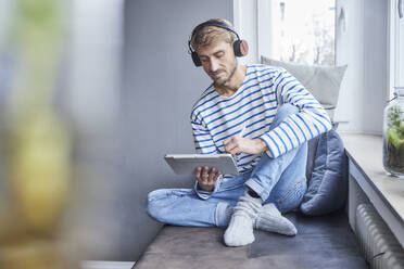 Businessman working with tablet PC sitting on sofa at home - FMKF07382