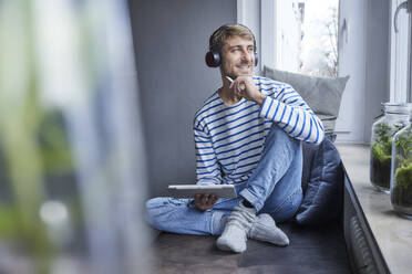 Smiling working man with tablet PC sitting on sofa at home - FMKF07384