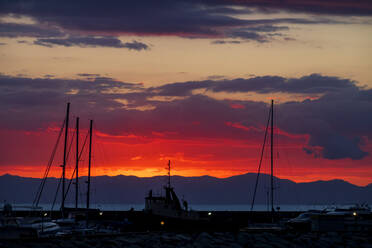 Italien, Provinz Südsardinien, Villasimius, Silhouetten von Booten im Küstenhafen bei rotem stimmungsvollem Sonnenuntergang - NDF01374