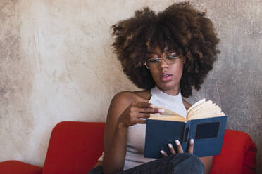 Young woman with afro hairstyle reading book at home - PNAF02652