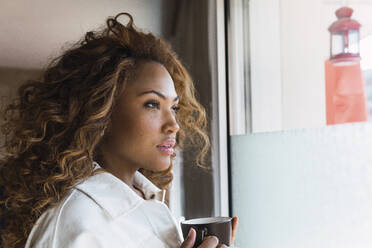Thoughtful woman with coffee cup looking out of window - PNAF02674