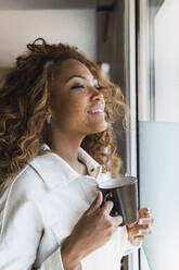 Woman holding coffee cup and looking out of window - PNAF02676