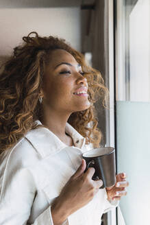 Frau hält Kaffeetasse und schaut aus dem Fenster - PNAF02676