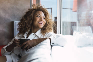 Happy woman holding coffee cup at home - PNAF02684