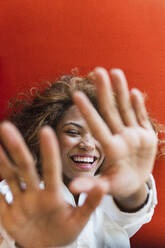 Happy woman showing stop gesture on sofa - PNAF02703