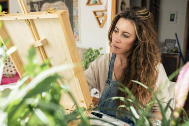 Konzentrierte Frau vor einer Staffelei, die zu Hause malt - MRRF01804