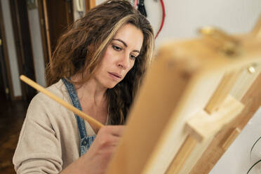 Woman with paintbrush painting at home - MRRF01805