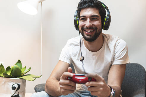 Fröhlicher Mann mit Kopfhörern, der zu Hause ein Videospiel spielt - JAQF01028
