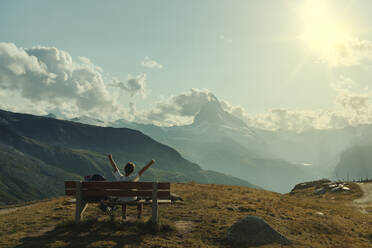 Junge mit ausgestreckten Armen auf einer Bank sitzend mit Blick auf das Matterhorn, Zermatt, Schweiz - LOMF01296