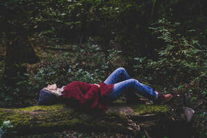 Woman lying on tree trunk in forest - SIPF02698