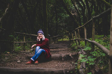 Smiling woman sitting on wooden path in forest - SIPF02701