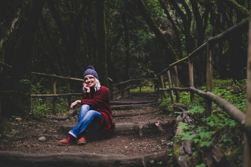 Lächelnde Frau sitzt auf einem Holzweg im Wald - SIPF02701