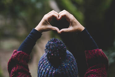 Woman making heart sign with hands in forest - SIPF02706