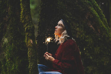 Nachdenkliche Frau mit Wunderkerze im Wald - SIPF02707