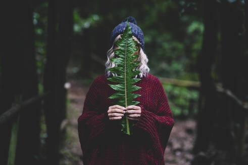 Frau versteckt Gesicht mit grünem Blatt im Wald - SIPF02710