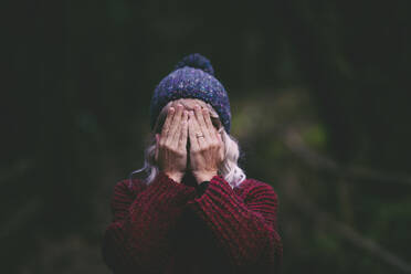 Woman covering face with hands in forest - SIPF02715