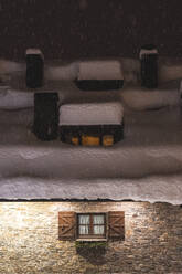 Snow falling outside brick house at night - JAQF01029