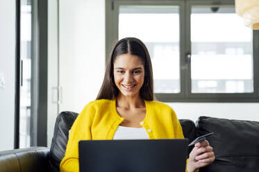 Glückliche Frau beim Online-Shopping am Laptop zu Hause - PGF00933