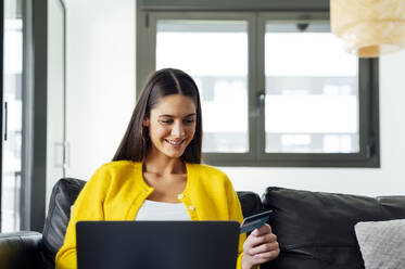 Lächelnde Frau mit Kreditkarte beim Online-Shopping am Laptop - PGF00934