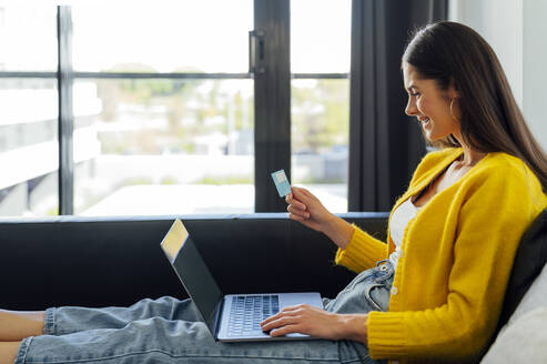 Glückliche Frau mit Kreditkarte beim Online-Shopping im Wohnzimmer - PGF00937