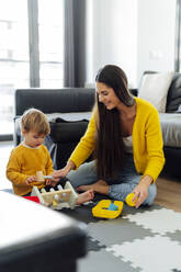 Lächelnde Mutter spielt mit ihrem Sohn im Wohnzimmer - PGF00943