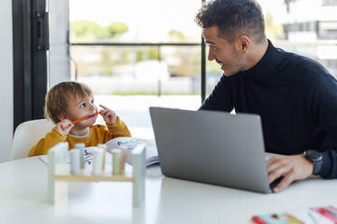 Vater spricht mit Sohn und arbeitet zu Hause am Laptop - PGF00949