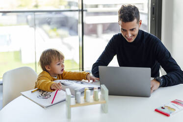 Smiling businessman freelancing on laptop by son at home - PGF00950