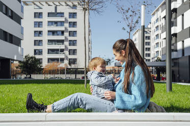 Cheerful mother playing with son on grass in the city - PGF00953