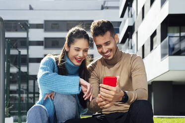 Smiling man sharing smart phone with woman on sunny day - PGF00964