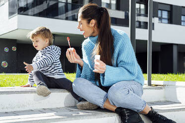 Cheerful mother and son playing with soap bubbles on sunny day - PGF00972