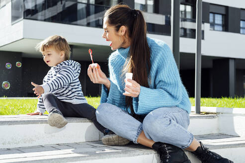 Fröhliche Mutter und Sohn spielen mit Seifenblasen an einem sonnigen Tag - PGF00972
