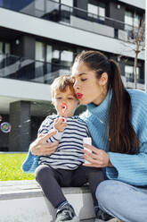 Mother and son blowing soap bubbles in city - PGF00973