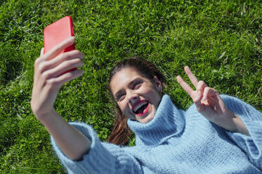 Fröhliche Frau, die im Gras liegend ein Selfie macht - PGF00975