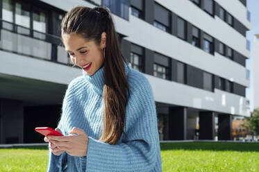 Lächelnde Frau, die an einem sonnigen Tag ihr Smartphone am Gebäude benutzt - PGF00978