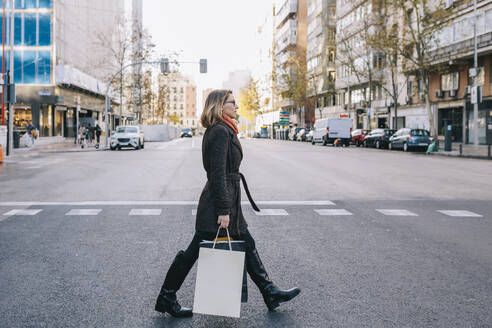 Woman with shopping bags crossing road in city - MRRF01822